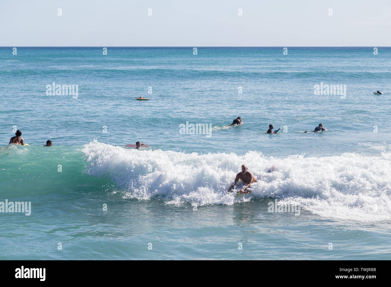 Eine Szene aus dem Strand. Ein Mann Ritt auf einer Welle von liegend auf seinem Surfbrett an die Ufer am Queen's Beach, Waikiki, Hawaii, USA. Stockfoto