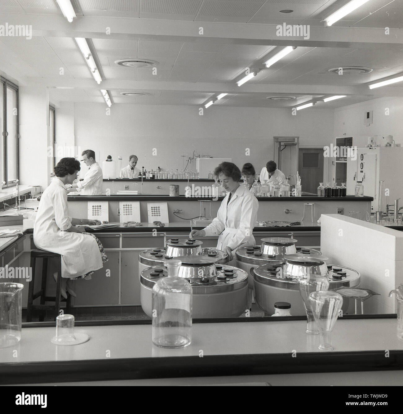 1950, historische, weibliche und männliche Wissenschaftler bei der Arbeit in einem brighly beleuchtet, modernes Labor an der chemcial Farbstoff Hersteller Sandoz, in Horsforth, Leeds, England, Großbritannien gebaut. Die Mitarbeiter sind Tests chemcial Farbstoffe für den Einsatz in der Textil- und Papierindustrie. Stockfoto
