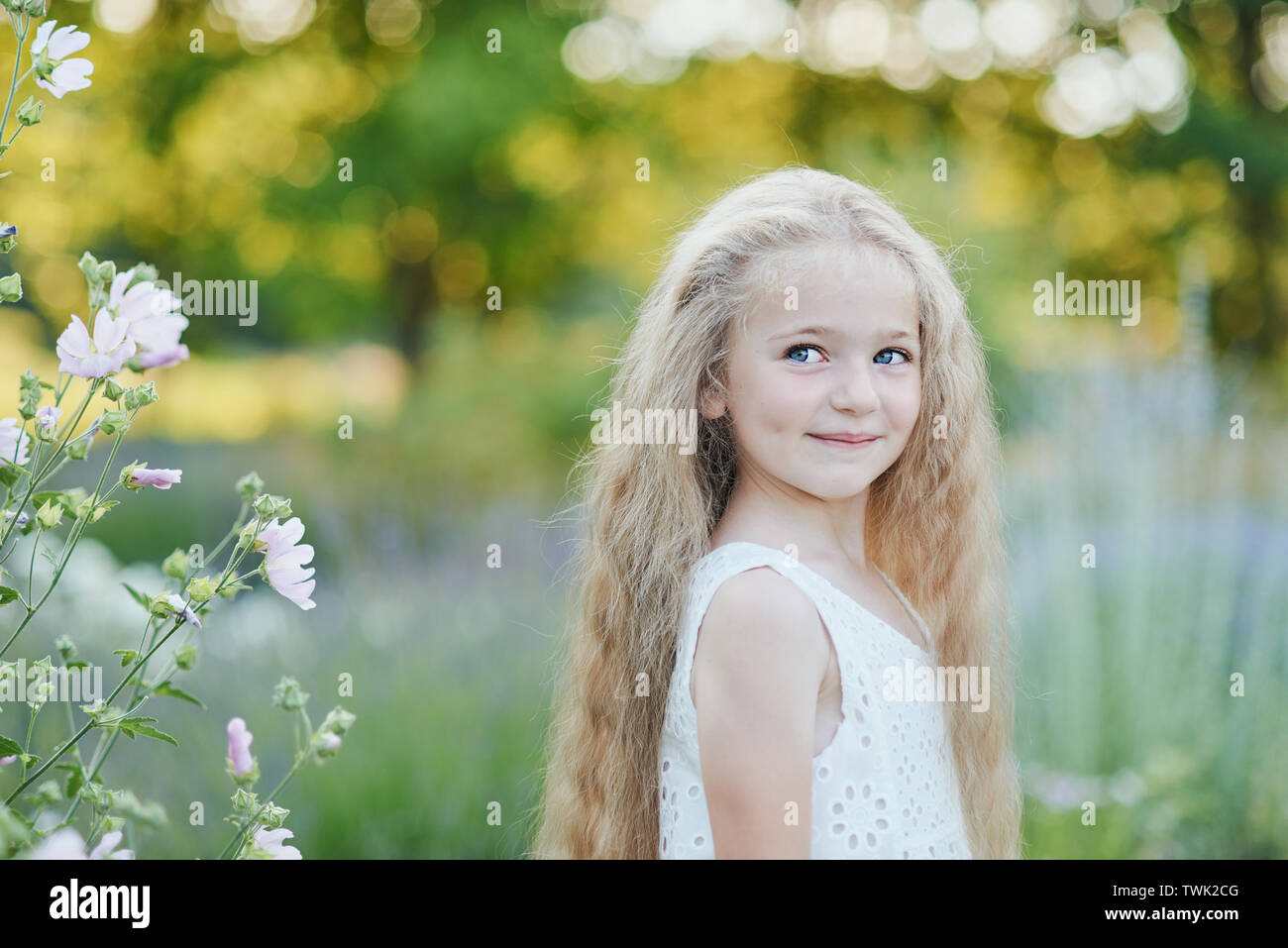 Close up Portrait von hübsch, blaue Augen, faire dunkelhäutige Mädchen mit glücklich und mit foxy Gesichtsausdruck und lange blonde Locken, Draußen, Hintergrundbeleuchtung auf hell Stockfoto