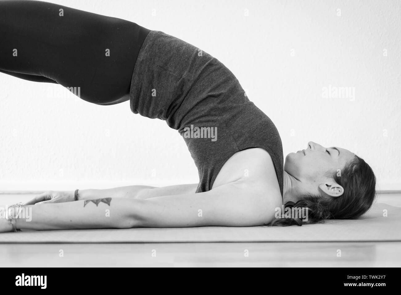 Seitenansicht einer jungen, brünetten europäischen Frau in ihren 30ern, die die Bridge Pose (Setu Bandhasana) auf einer Yoga-Matte, einem rückwärtsbiegenden Yoga-Asana, praktiziert Stockfoto