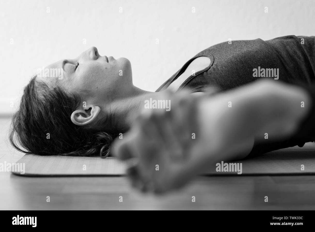 Bodennahe, schwarz-weiße horizontale Nahaufnahme einer jungen brünetten europäischen Frau, die im Innenraum liegend Straddle Pose oder Supta Samakonasana spielt. Stockfoto