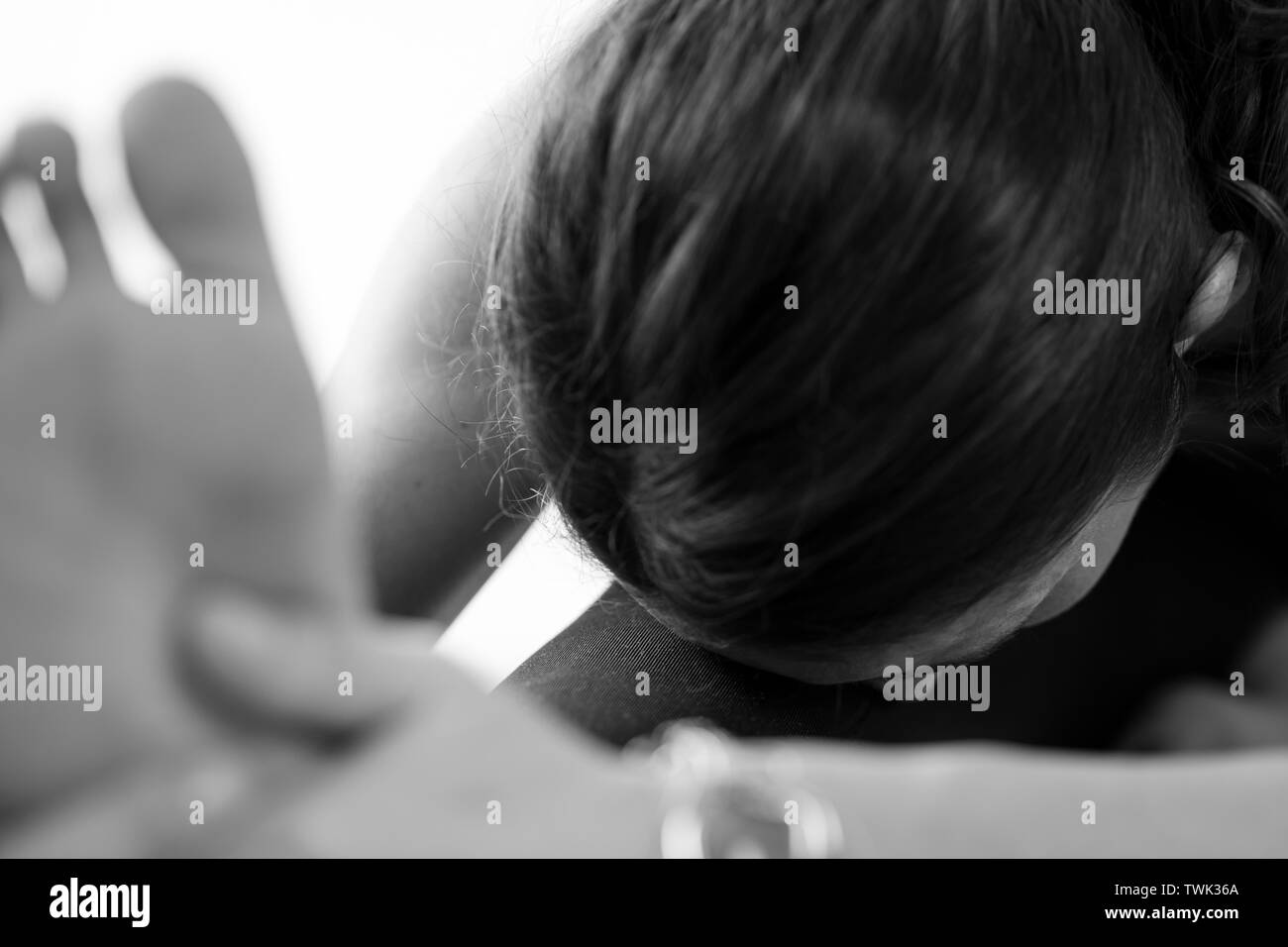 Nahaufnahme einer nicht erkennbaren brünetten Europäerin auf dem Boden, die Janu Sirsasana oder Kopf-zu-Knie-Vorwärtsbeugung auf schwarz-weißem Boden übt Stockfoto