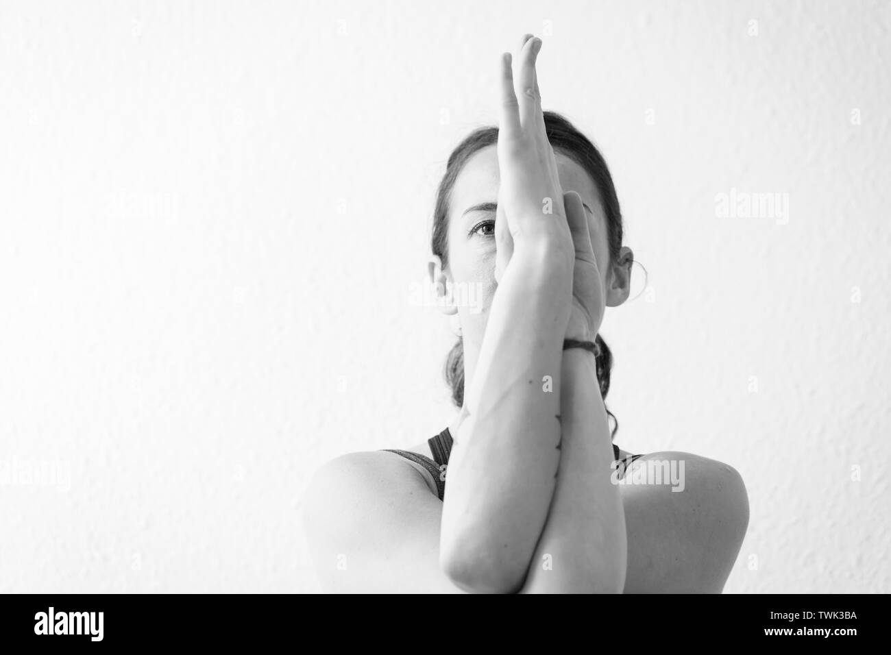 Nahaufnahme, schwarz-weiß Vorderansicht einer brünetten Frau in ihren 30ern mit offenen Augen, die sitzende Adleryoga Pose Arme oder Garudasana. Horizontales Format Stockfoto