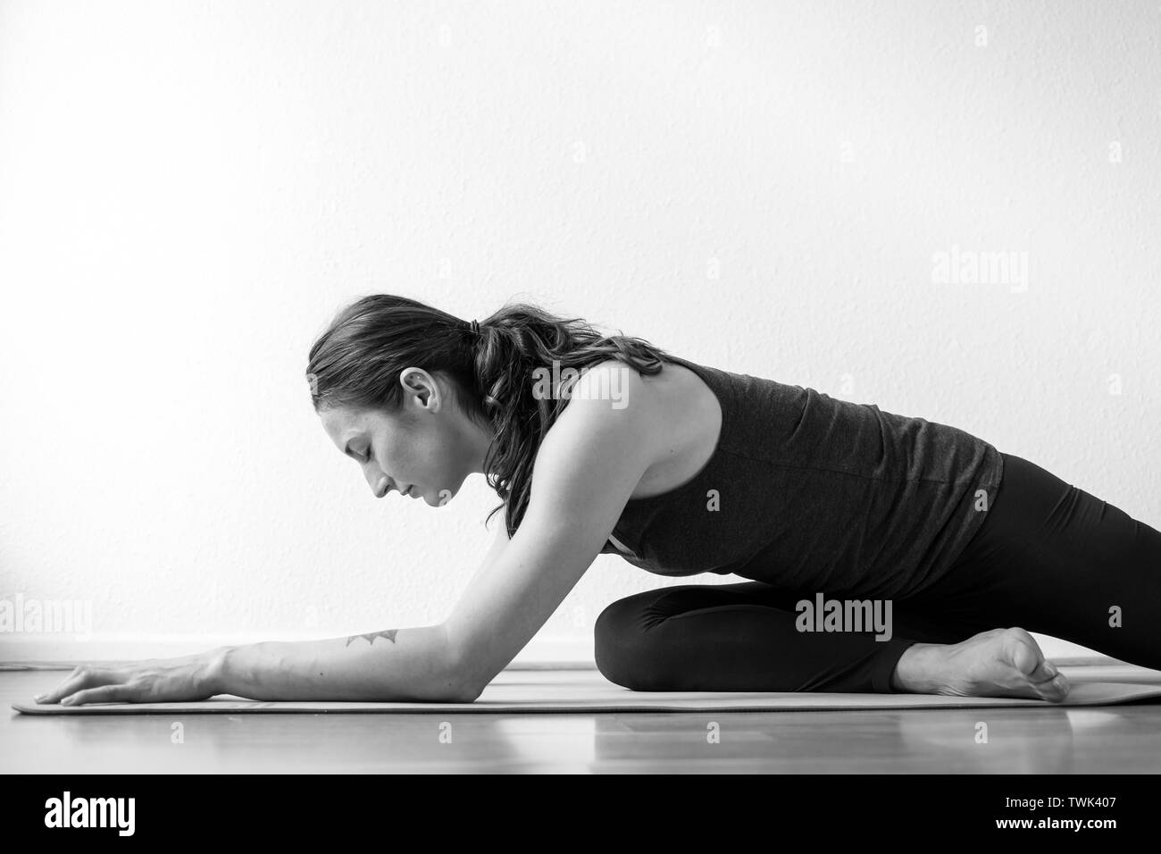 Die Seitenansicht einer jungen Frau, die zu Hause arbeiten in der Nähe, die schlafende Swan Yin Yoga Haltung, mittlere Länge. Stockfoto