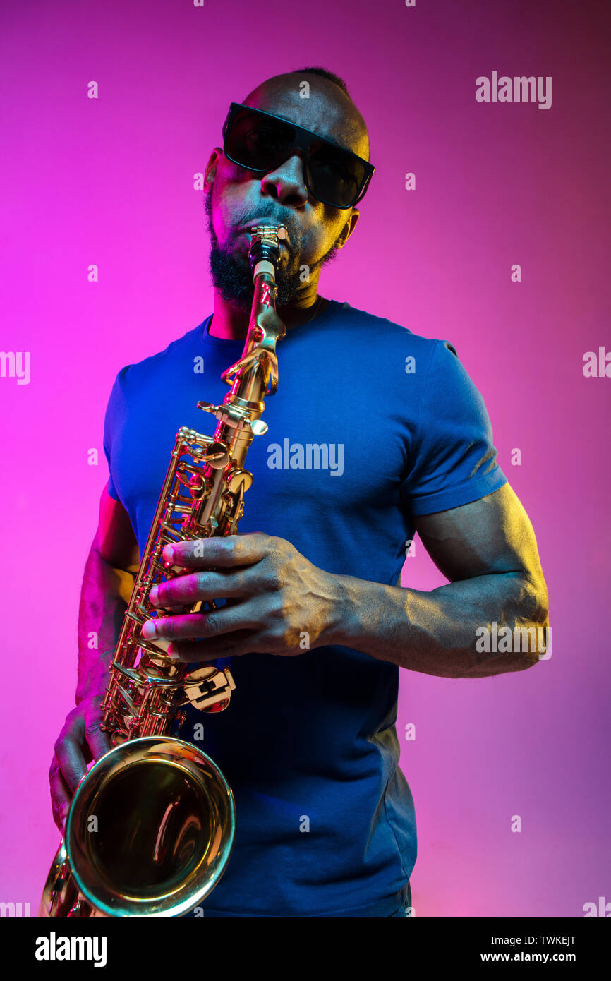 Junge afrikanische-amerikanischen Jazz musiker Saxophon auf Pink Studio  Hintergrund in trendigen Neon Licht. Konzept der Musik, Hobby. Freudige  attraktiver Kerl improvisieren. Bunte Porträt des Künstlers Stockfotografie  - Alamy