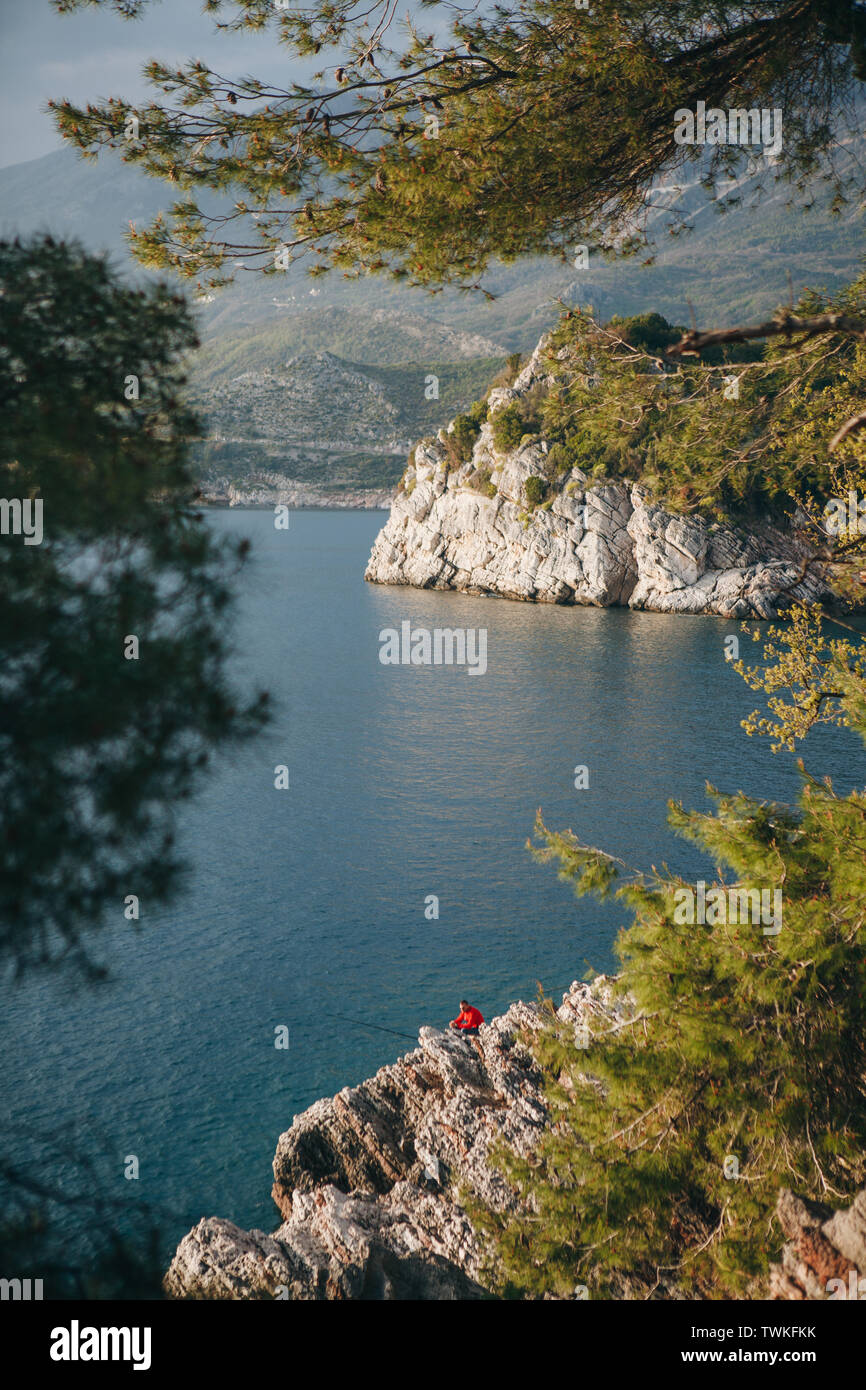 Schönen Blick durch die Bäume auf das Meer und die Landschaft. Zu den felsigen Küsten der eine nicht erkennbare Mann angeln. Stockfoto