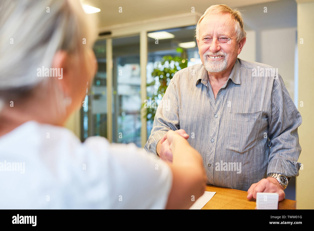 Senior als Patient auf Begrüßung mit handschlag an der Rezeption beim Arzt oder Physiotherapeuten Stockfoto