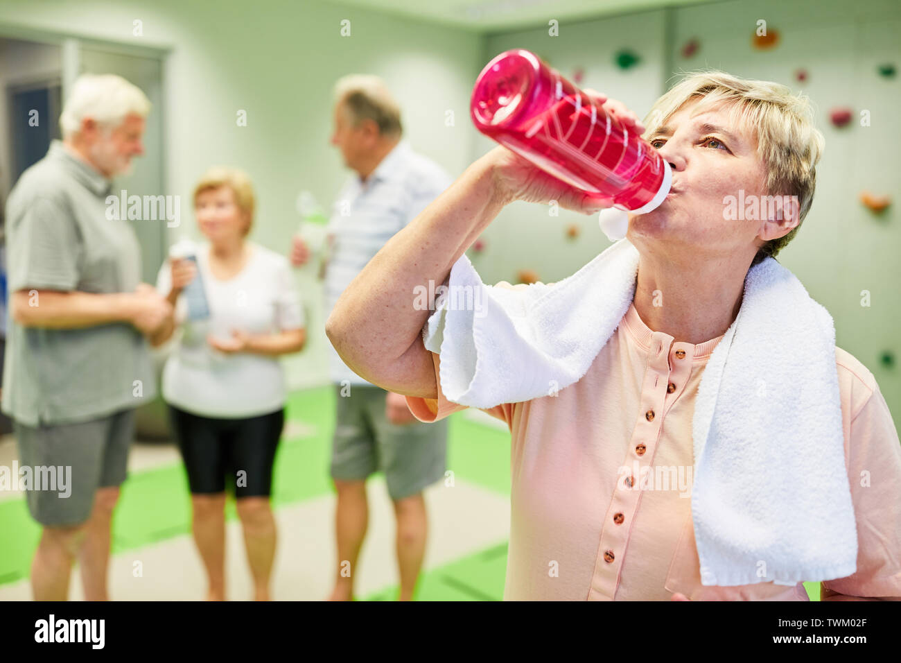 Ältere Frau trinkt Wasser aus einer Flasche während einer Pause während der Fitness Training in der Kletterhalle Stockfoto
