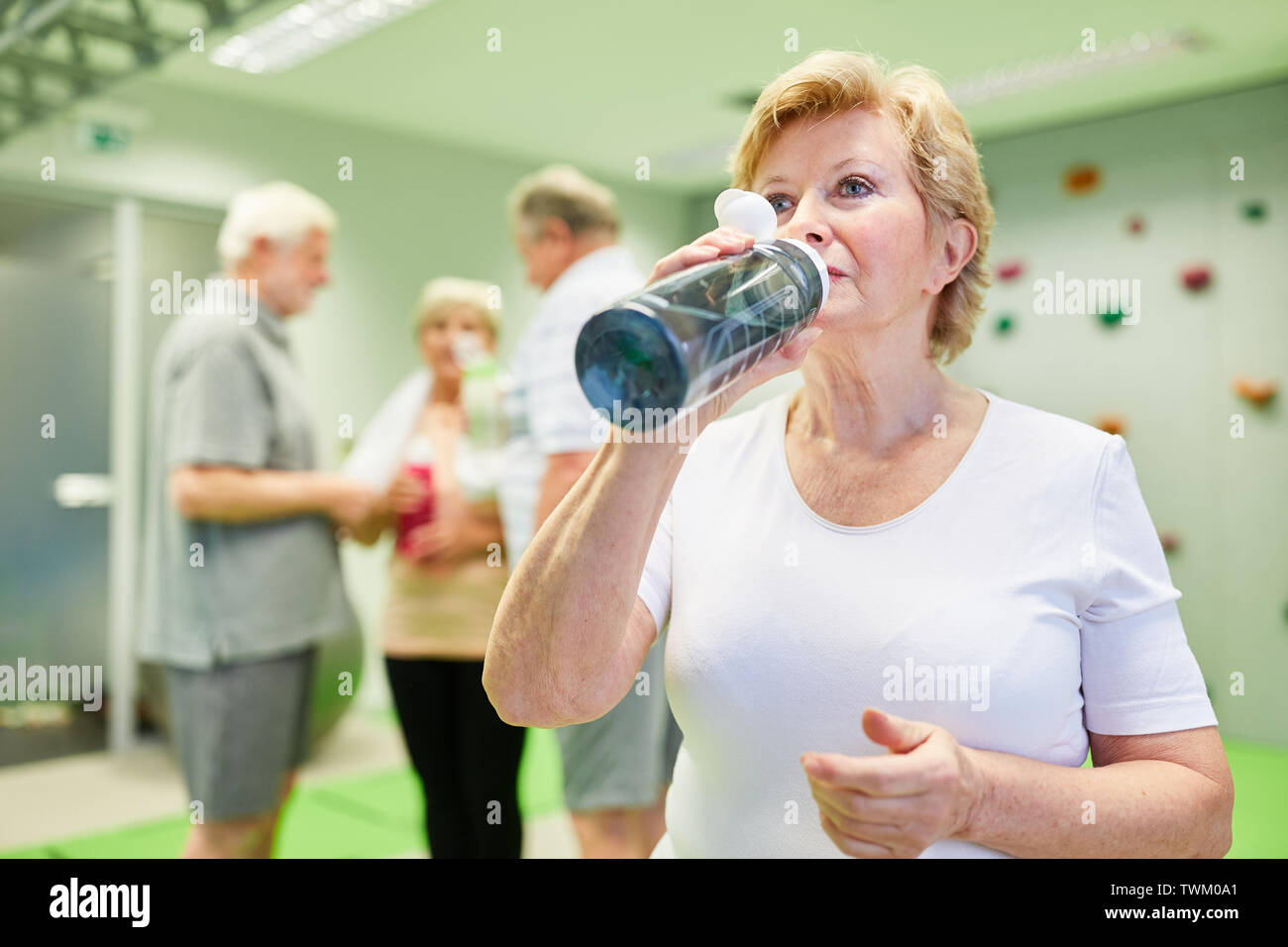 Ältere Frau trinkt Wasser aus einer Flasche für Erfrischung nach dem Sport in der Kletterhalle Stockfoto