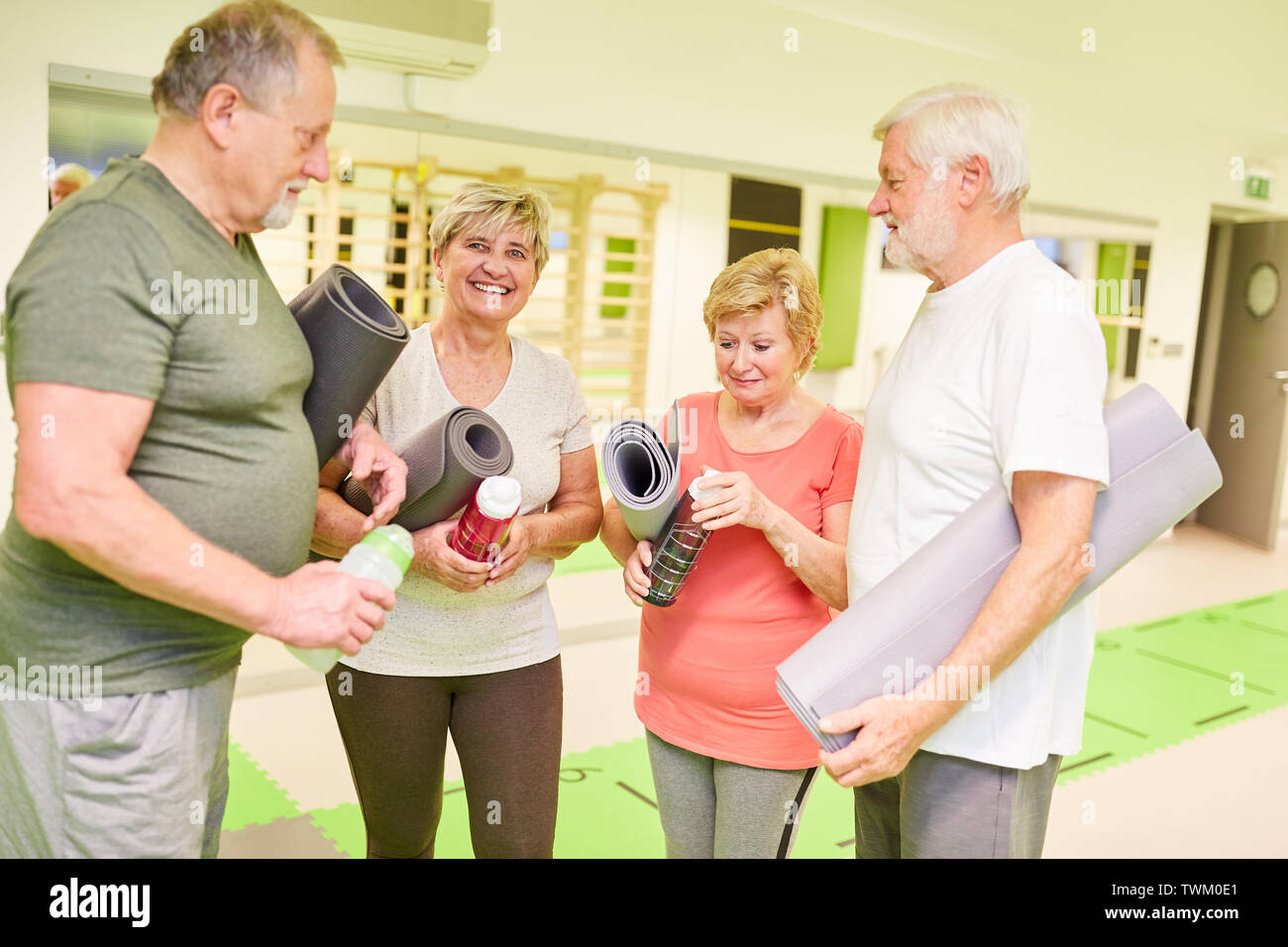 Gruppe von Seniorinnen und Senioren mit Yoga Matte im Fitnesscenter während einer Pause während der small talk Stockfoto