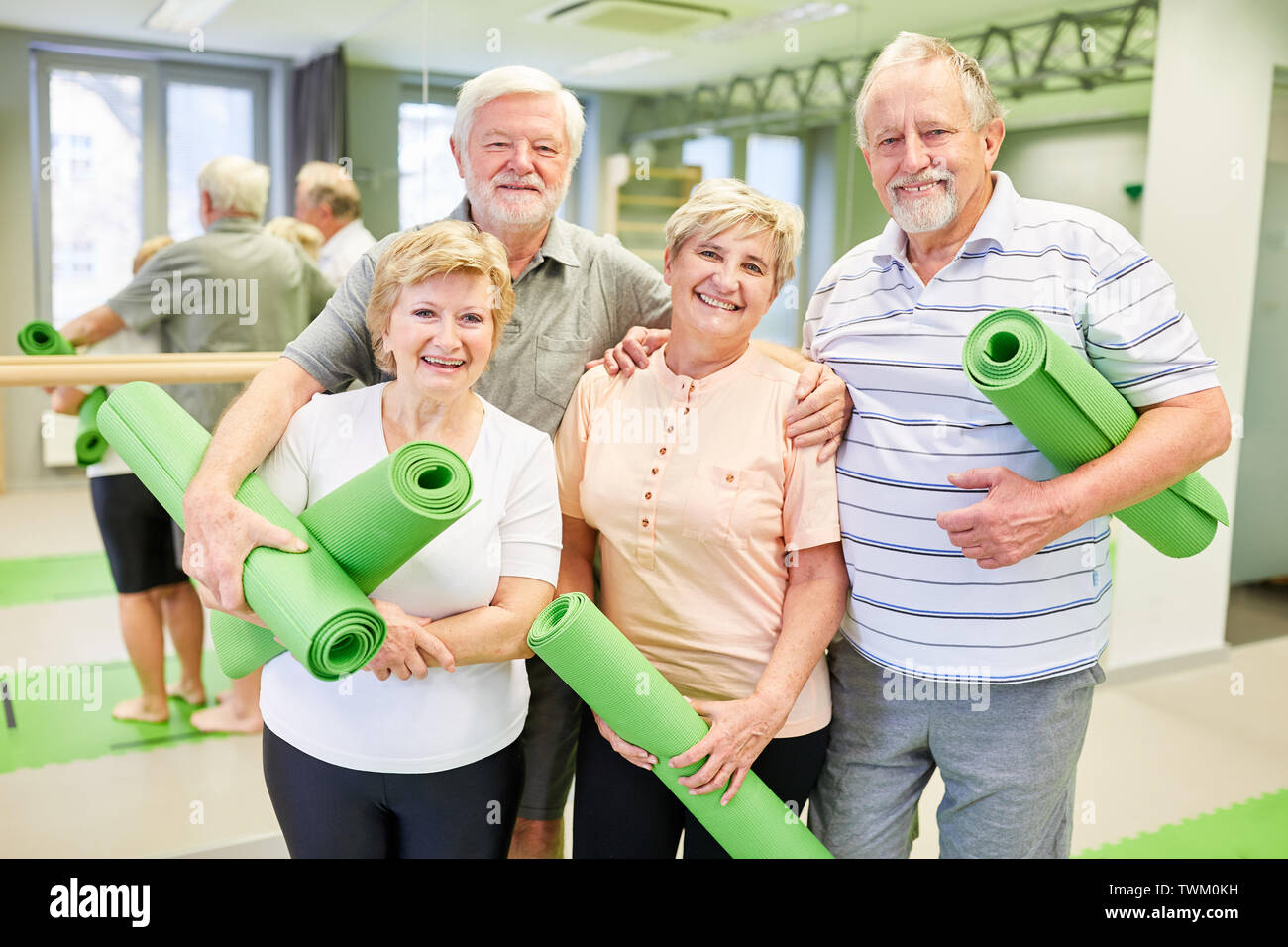 Sportliche Senioren als Freunde mit Yoga Matte freuen sich auf Gymnastik Klasse im Fitnesscenter Stockfoto