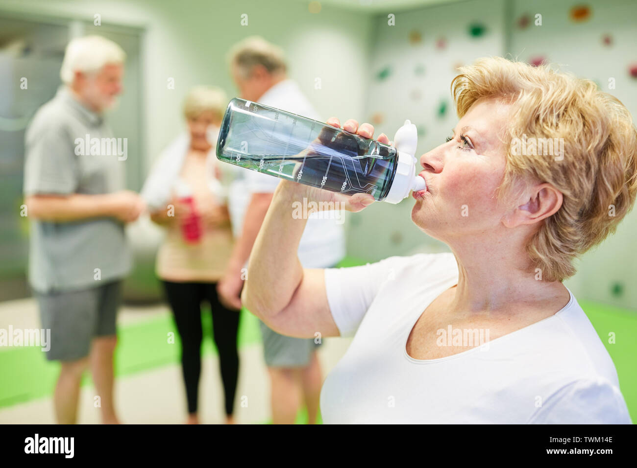 Vital senior Frau stillt ihren Durst mit Wasser nach dem Fitness Training in der Kletterhalle Stockfoto