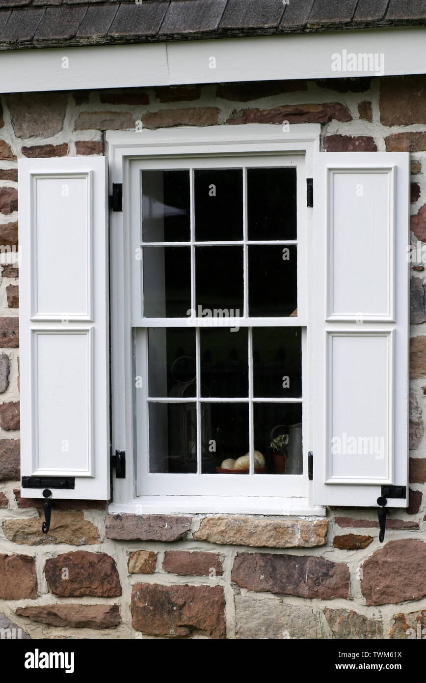 Das Steinhaus ist mit weißen Fensterläden aus Holz am Fenster. Stockfoto