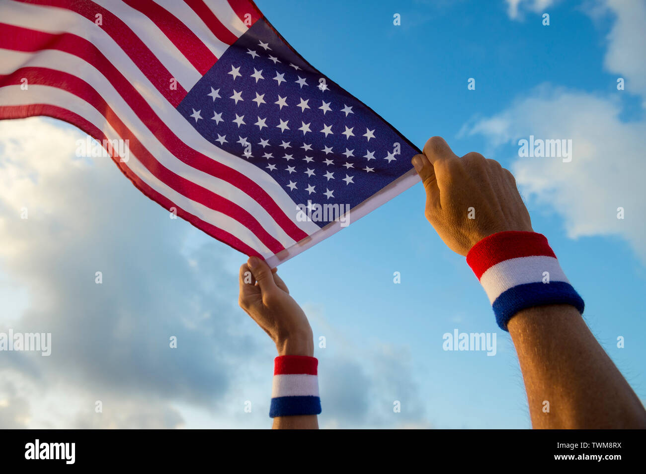 Hand mit USA roten, weißen und blauen Armbänder Holding eine amerikanische Flagge schwenkten in hellen, sonnigen blauen Himmel Stockfoto