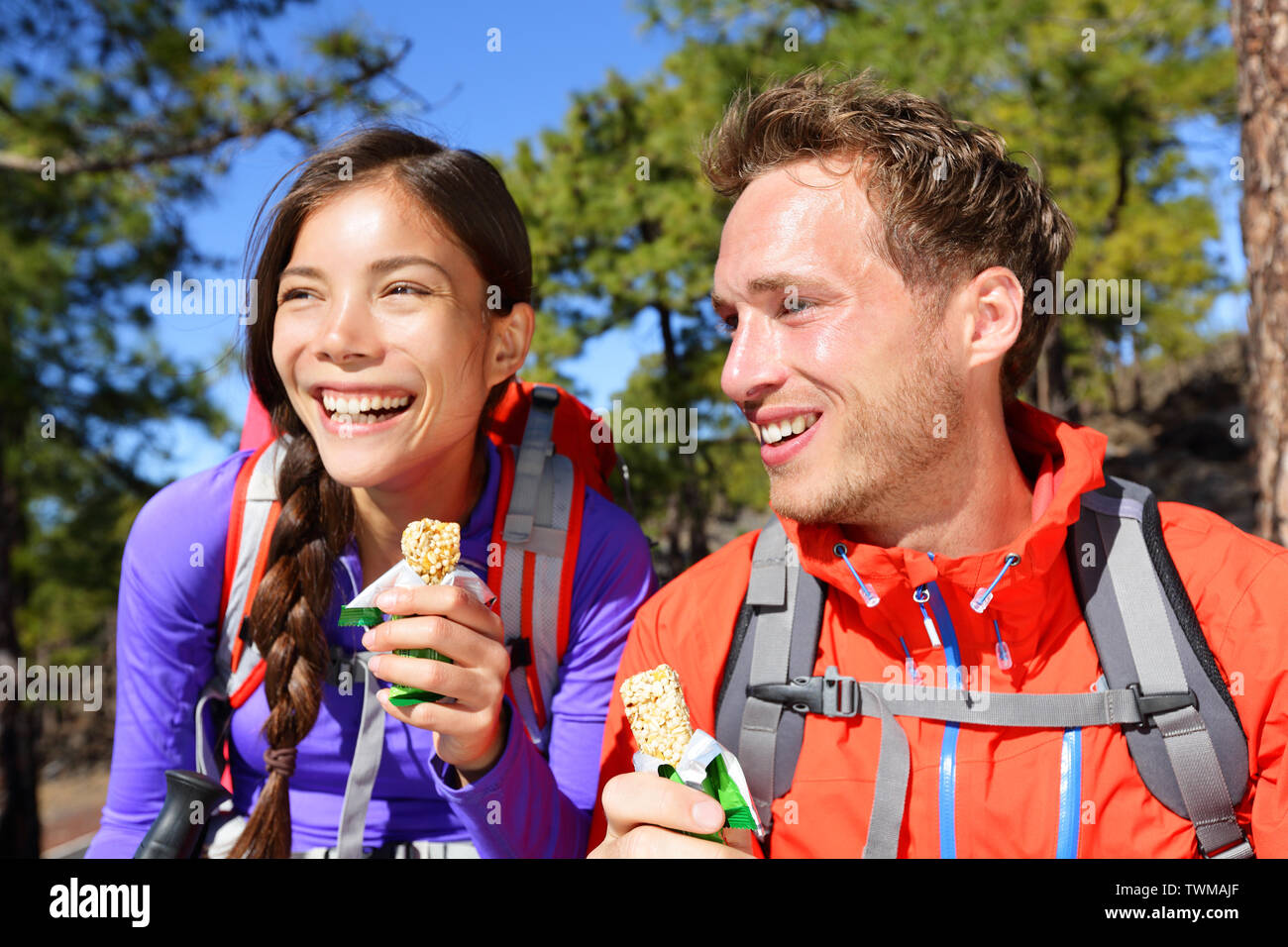 Paar essen Müsliriegel wandern. Glückliche Menschen genießen Müsli Müsliriegel, gesunden, aktiven Lebensstil in der Bergnatur. Frau und Mann Wanderer sitzen lachend während der Wanderung. Stockfoto