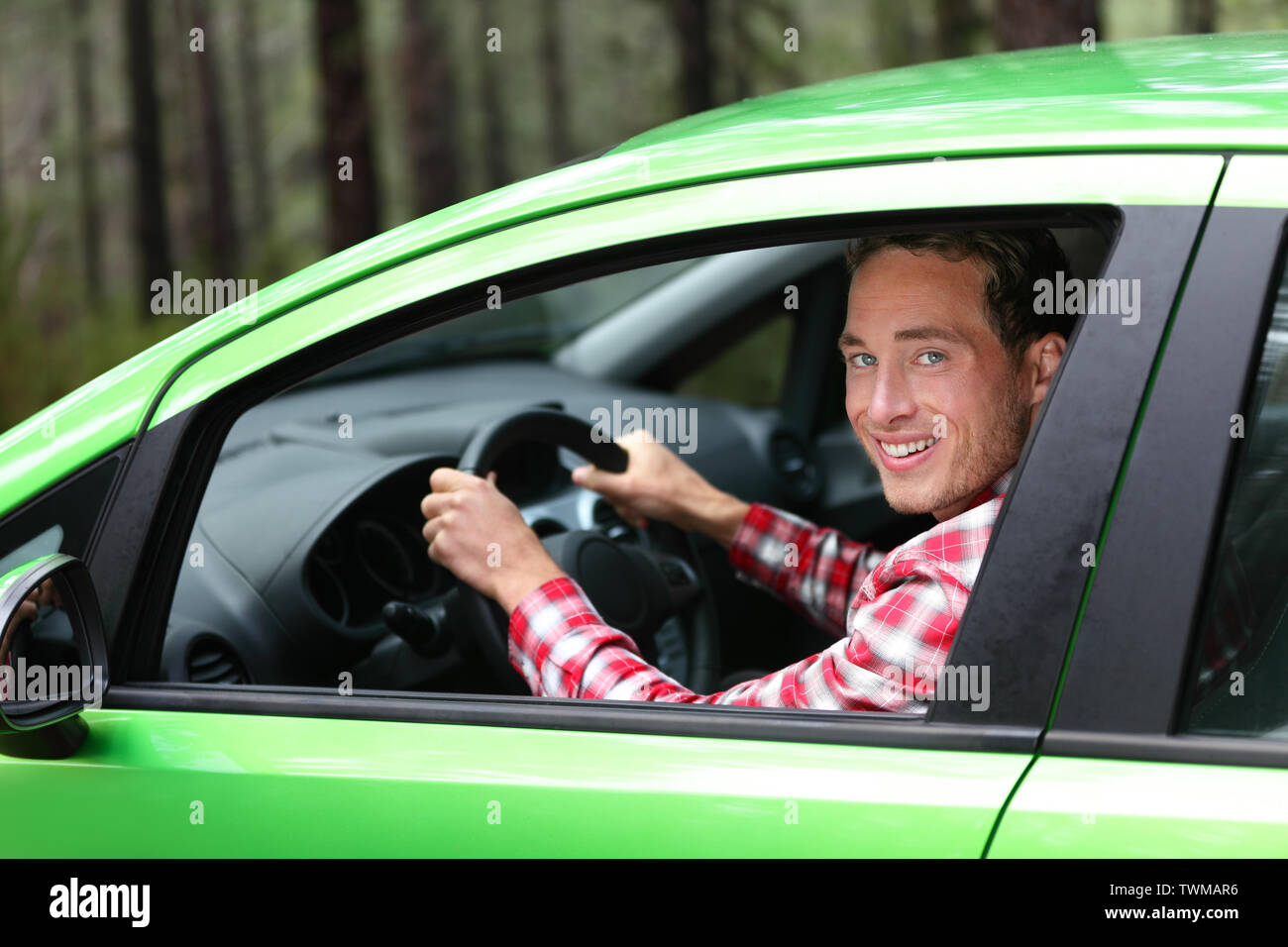 Elektrische Auto fahrer - grüne Energie Biokraftstoff Konzept. Männliche hinter Rad. Mann, der neuen Fahrzeug in fröhlichen Natur Wald. Junge männliche Fahrer auf Kamera mit Arm angehoben zujubeln. Stockfoto