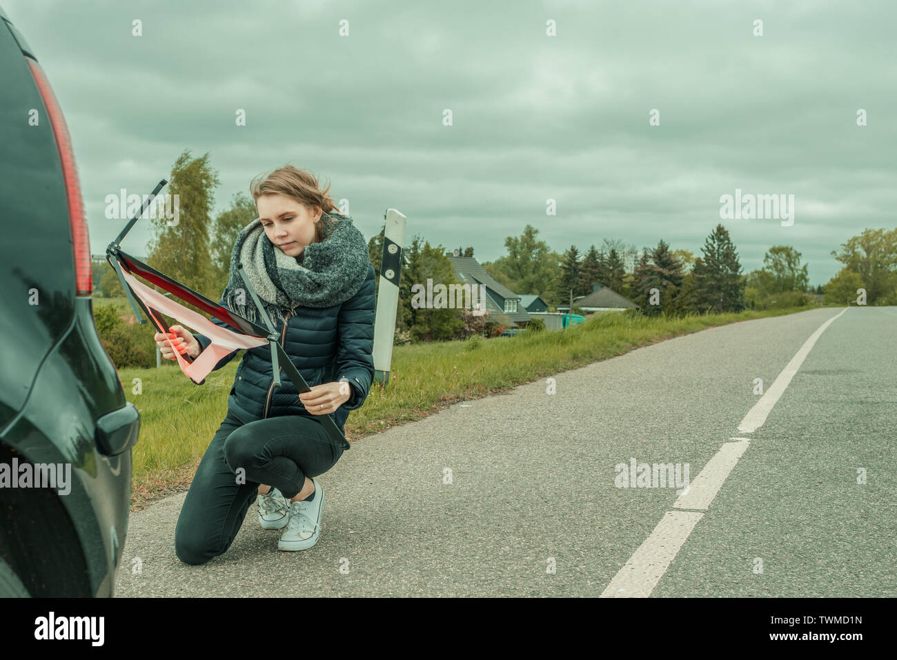 Eine junge Frau mit einer Autopanne versucht das Warndreieck zu montieren Stockfoto