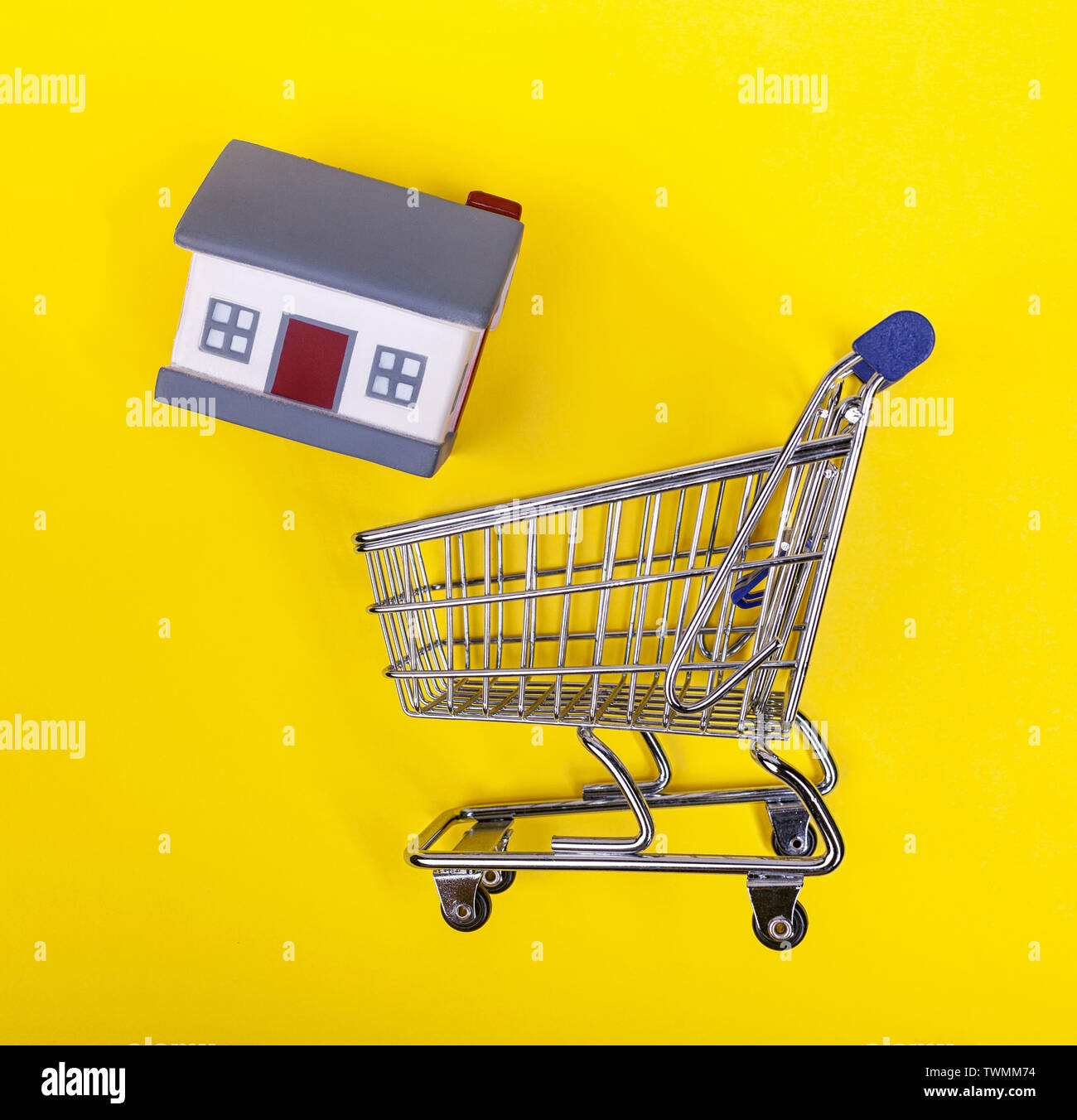Ein Supermarkt Warenkorb mit Gummi Häuser auf einem gelben Hintergrund. Das Konzept der Home Shopping und Marketing, Handel und Gewerbe. Stockfoto