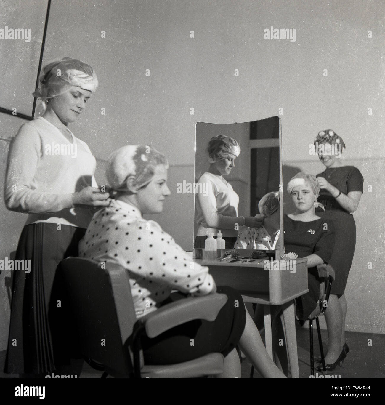 1960, historische, bei einem Friseur Schule oder Hochschule, zwei junge Lady's Sitzen auf Stühlen gegenüber Spiegel mit ihrem Haar in den Netzen von zwei Studentinnen, England, UK vorbereitet. Stockfoto
