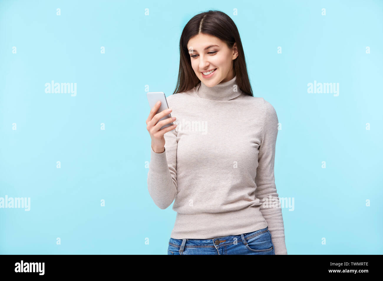 Schönen jungen kaukasischen Frau am Handy suchen, glücklich und lächelnd, auf blauem Hintergrund. Stockfoto