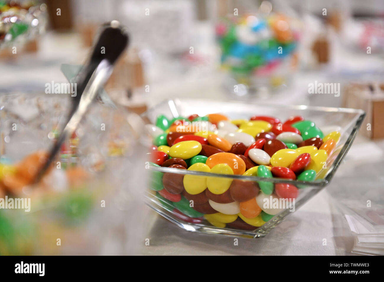 Glas Schale mit bunten Schokolinsen in den Farben des Regenbogens wird auf einen Tisch mit selektiven Fokus Stockfoto