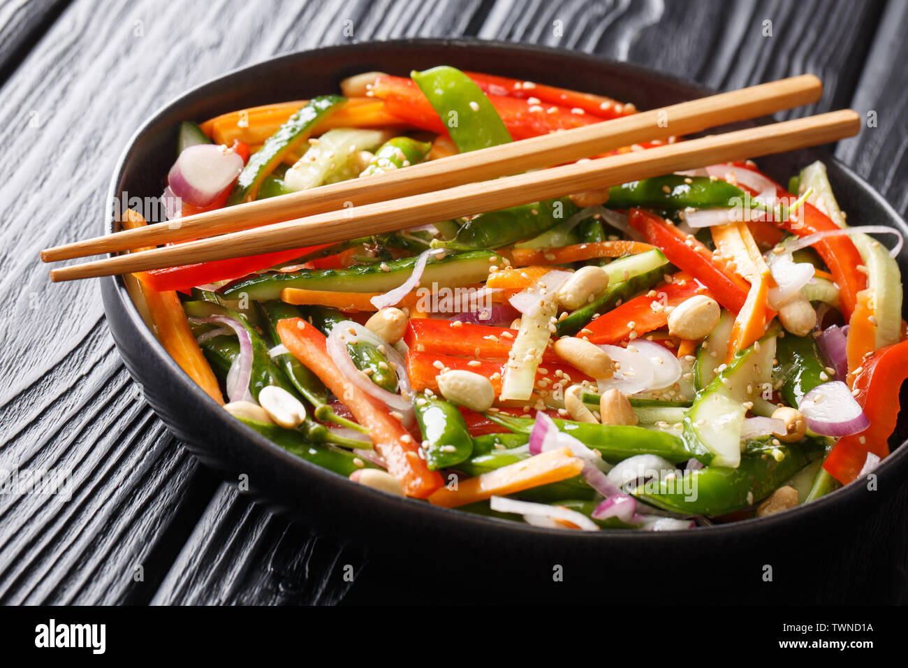 Salat mit Gurken, Paprika, Karotten, pea Pods mit Sesam und Erdnüsse close-up auf einem Teller auf den Tisch. Horizontale Stockfoto
