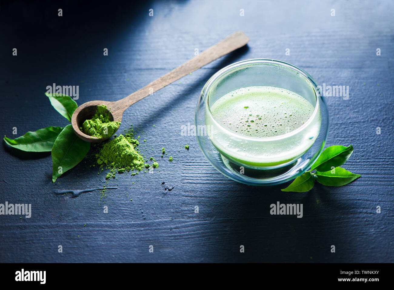 Matcha Tee mit Schaumstoff in eine doppelte Wand Glas mit einem Löffel aus Holz mit Matcha Pulver auf einem dunklen Hintergrund mit Kopie Raum Stockfoto