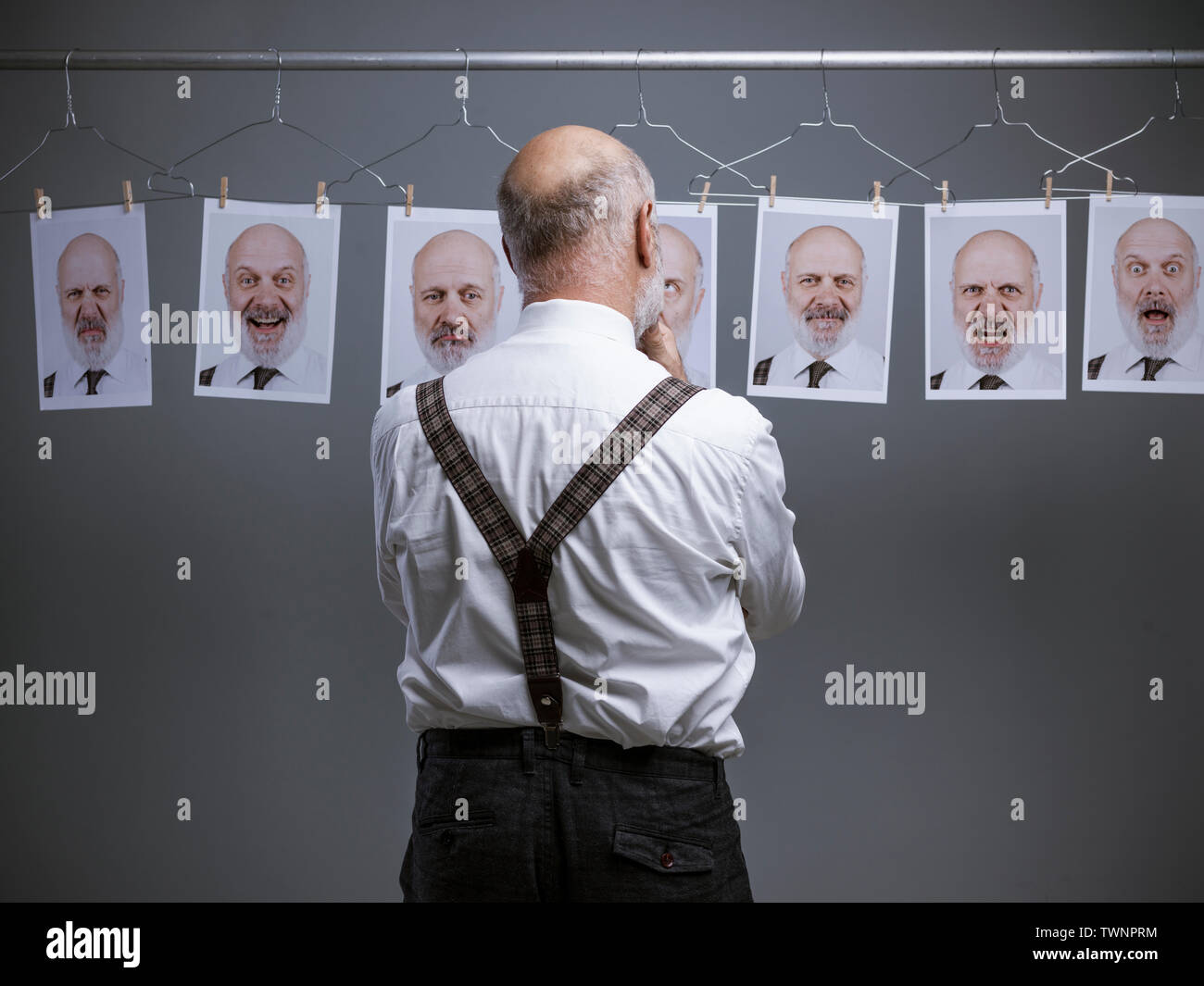 Reifen Geschäftsmann an seinem multiple Persönlichkeiten und Ausdrücke starrte auf eine Sammlung von hängenden Porträts: verstand Selbstanalyse und Emotionen Konzept Stockfoto