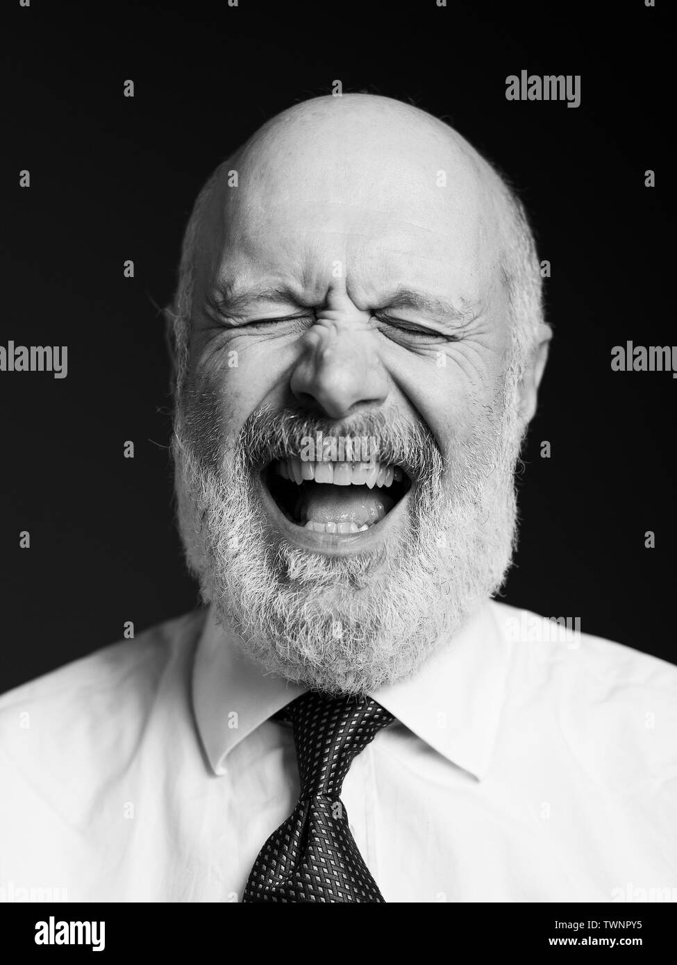 Fröhlichen älteren Geschäftsmann auf schwarzen Hintergrund posiert, ist er stirnrunzelnd mit geschlossenen Augen und Lachen Stockfoto