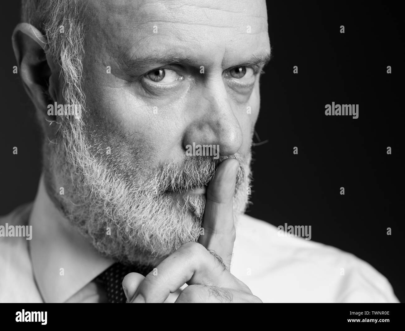 Zuversichtlich Geschäftsmann auf schwarzem Hintergrund posiert und auf Kamera, er hält den Finger auf die Lippen und bitten um Ruhe Stockfoto