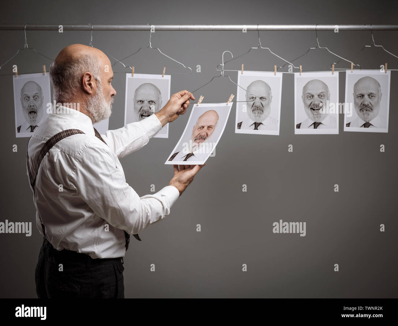Reifen Geschäftsmann an seinem multiple Persönlichkeiten und Ausdrücke starrte auf eine Sammlung von hängenden Porträts: verstand Selbstanalyse und Emotionen Konzept Stockfoto