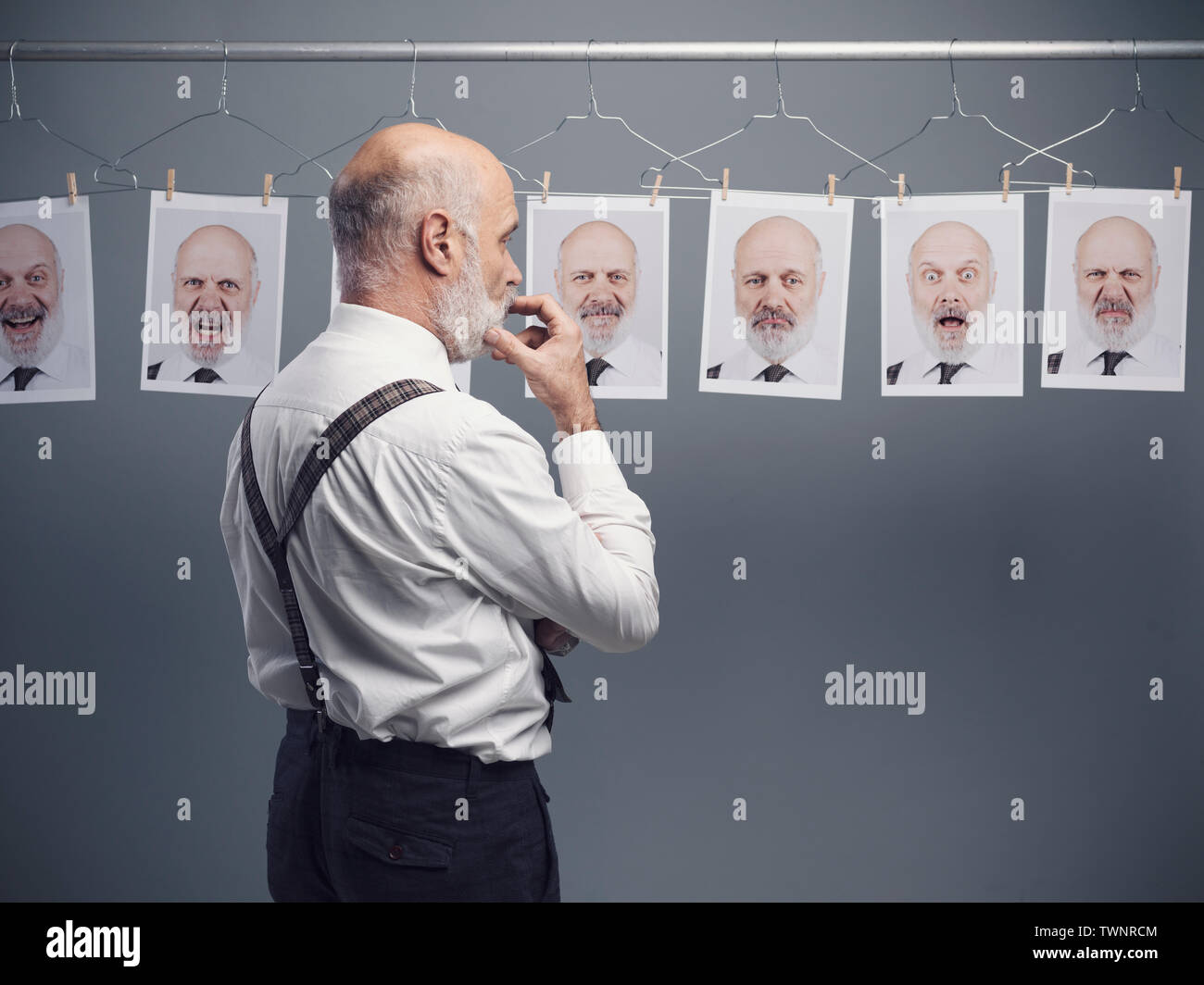 Reifen Geschäftsmann an seinem multiple Persönlichkeiten und Ausdrücke starrte auf eine Sammlung von hängenden Porträts: verstand Selbstanalyse und Emotionen Konzept Stockfoto