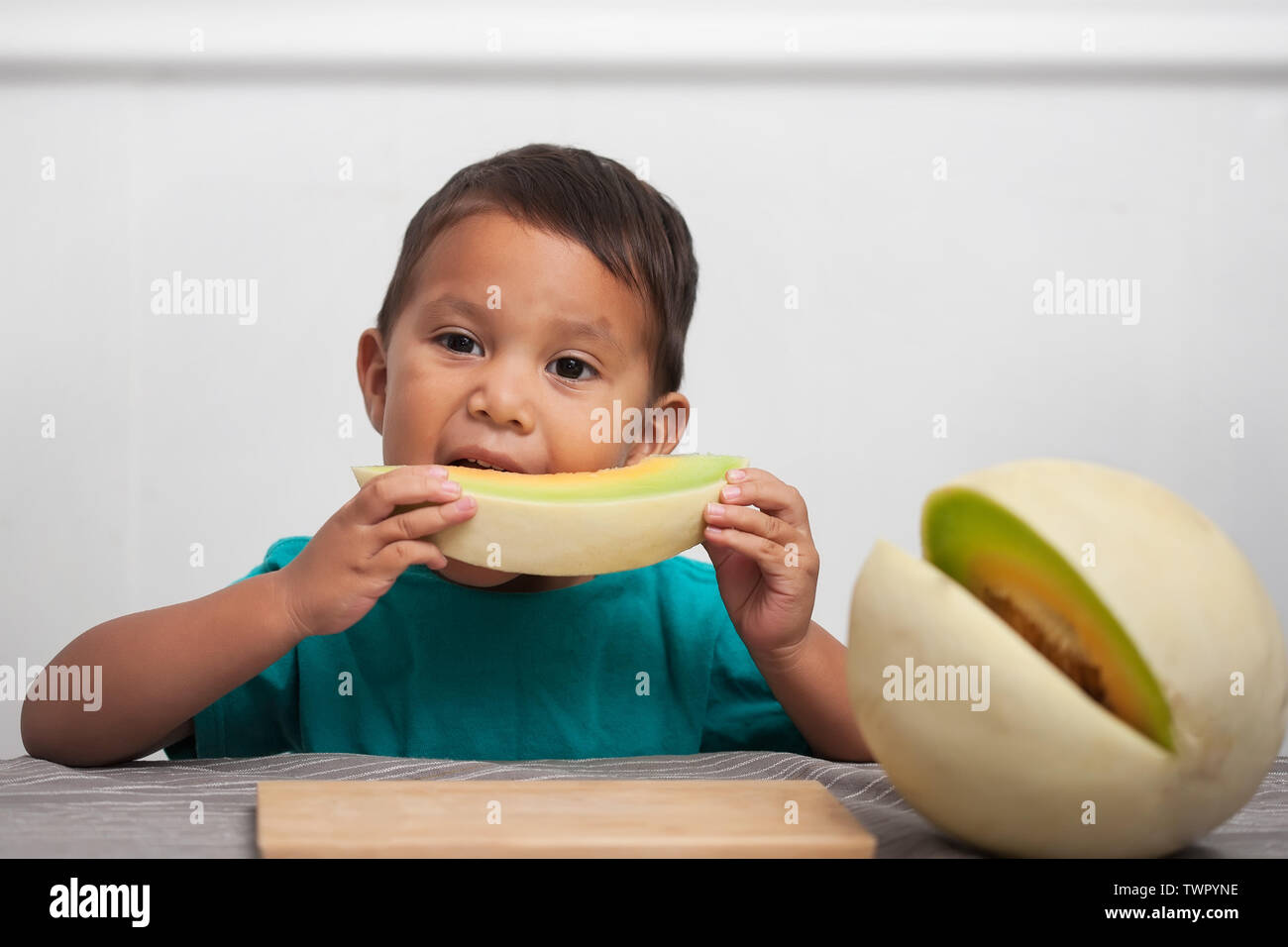 Ein Kind essen ein Stück frisches Obst honeymelon auf seinem eigenen und genießen eine gesunde Alternative zu verarbeiteten Lebensmitteln. Stockfoto