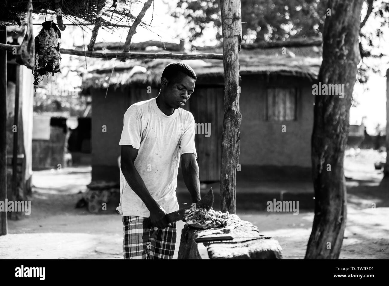 Eine Straße Metzger schneiden ein Stück Fleisch mit seinem panga Messer vor einer Hütte Stockfoto