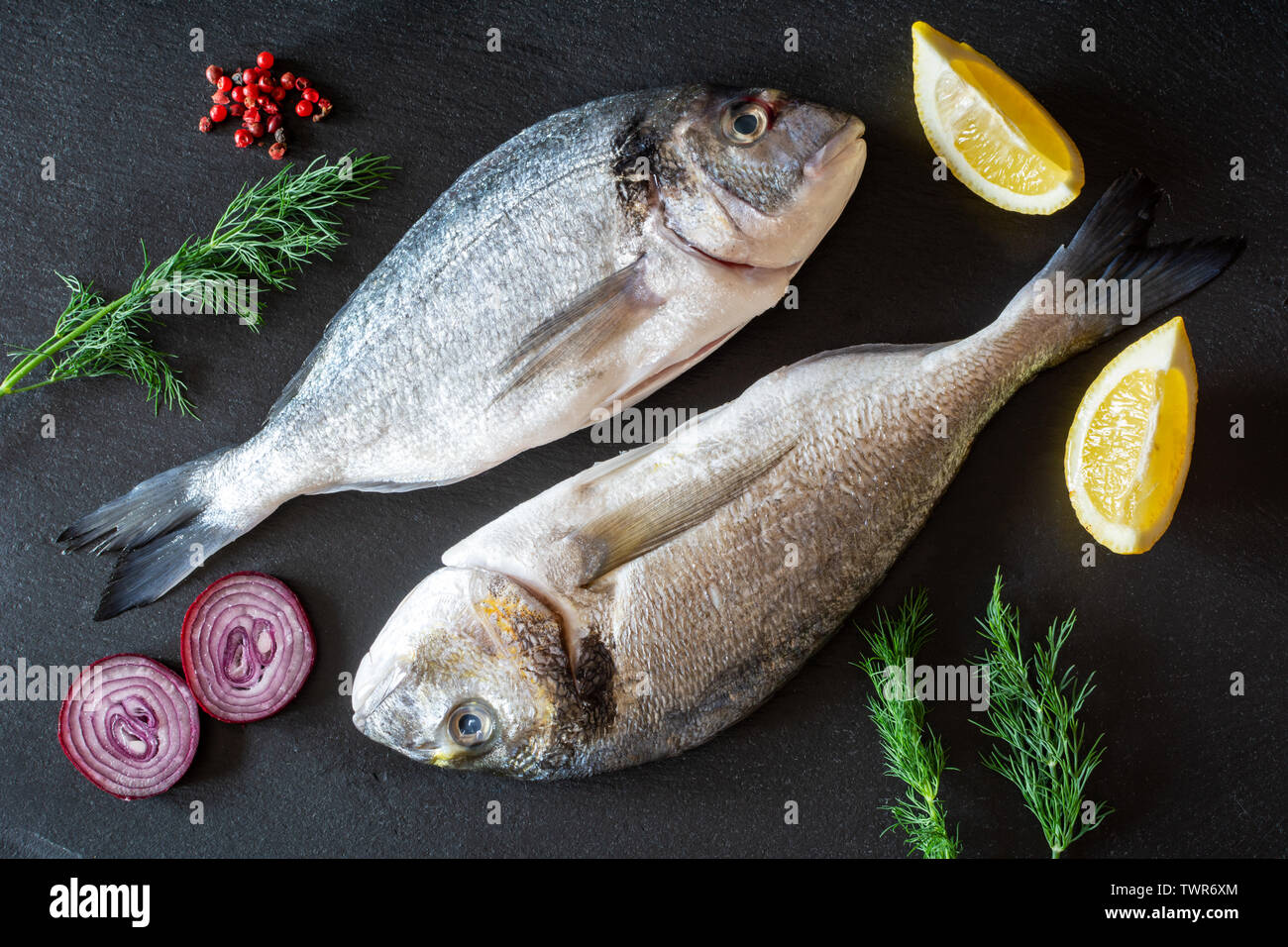 Frische rohe dorado Fisch mit Gemüse auf schwarzem Teller serviert. Stockfoto