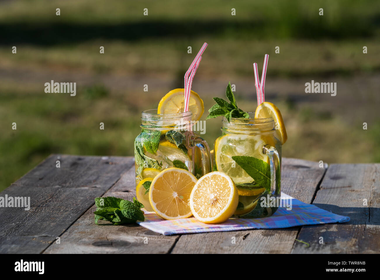 Nicht-alkoholische Getränke. Hausgemachte Limonade mit Zitrone, Minze und Eis, in einer Brille, über alten Holztisch, Outdoor, verschwommen grünen Hintergrund. Stockfoto