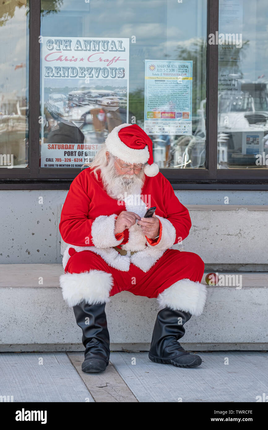 Santa Clause sein Handy während einer Pause bei der jährlichen Weihnachten im Juni Feier in Orillia Ontario Kanada prüfen. Kontrolle nughty schöne Liste. Stockfoto