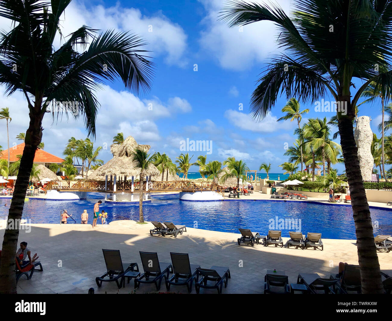 Blick auf den Pool vom Balkon aus mit einer Familie in der Wasser- und einem strohgedeckten Insel in der Mitte Stockfoto