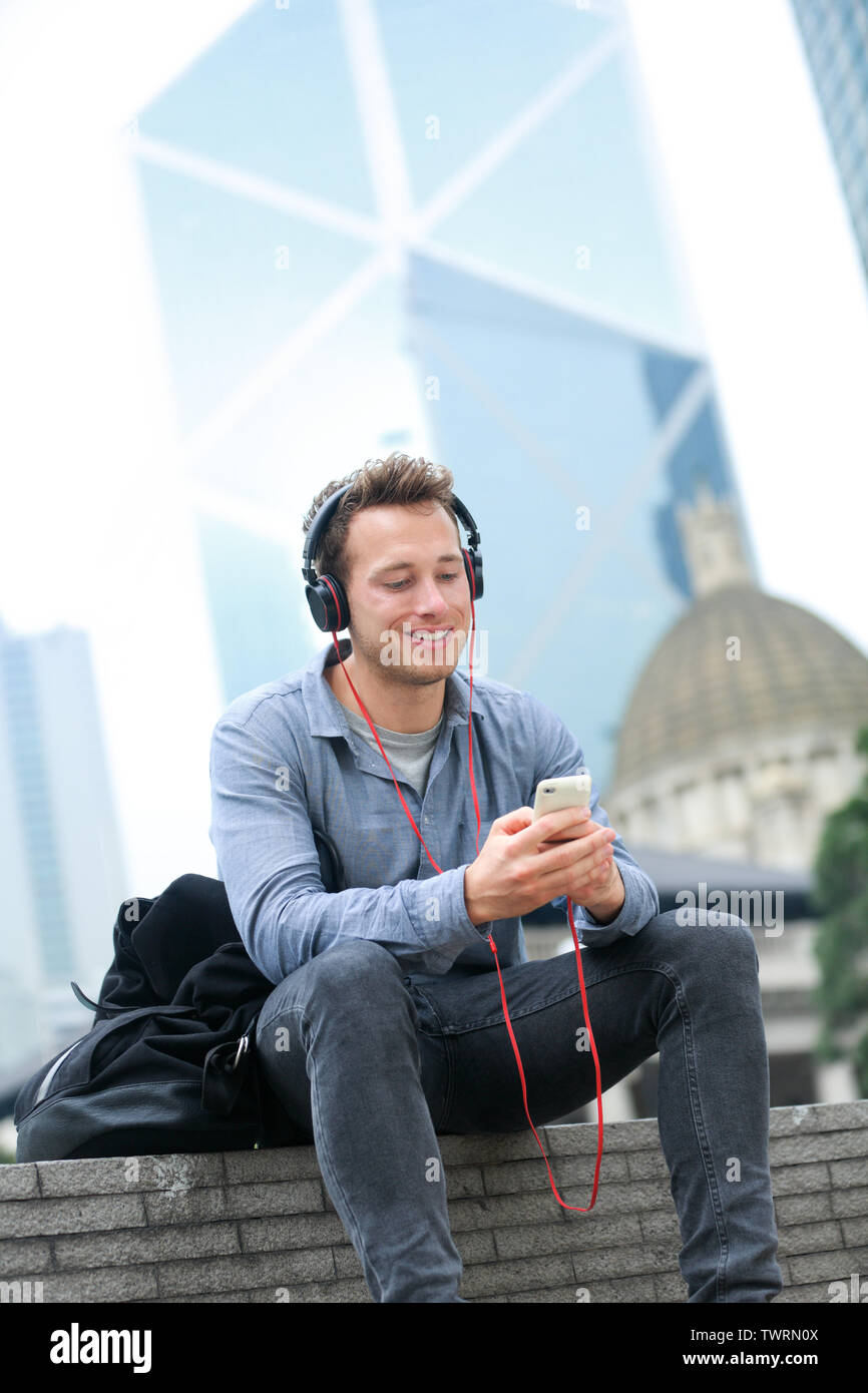 Urban Mann auf smart phone mit Kopfhörern hören von Musik oder Video Gespräch mit App sitzen auf 4G-Smartphones chatten. Casual Young Urban professional männlich in Hong Kong Central. Stockfoto