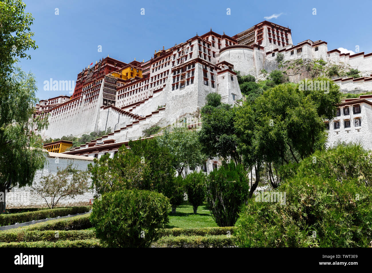 Seite Blick auf den Potala Palast mit bue Himmel. Im Vordergrund Bäume und Sträucher. Unesco Weltkulturerbe und Zentrum des tibetischen Buddhismus. Stockfoto