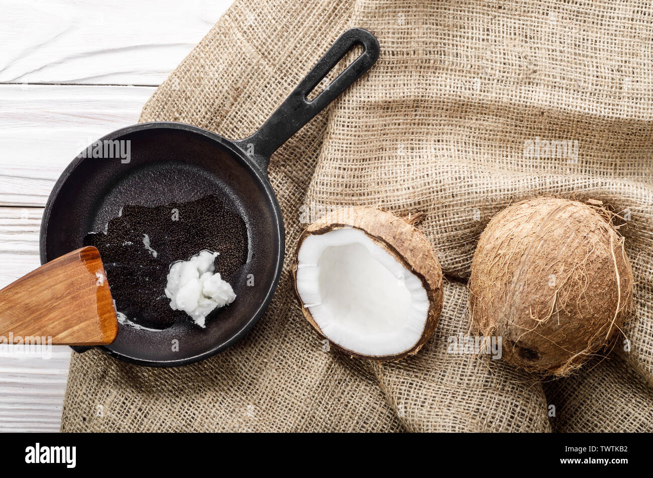 Kokosnuss, Shell mit Fleisch, Gusseisen Skillet und Spachtel auf Hanf Sack auf weißen Küche aus Holz Tisch Stockfoto