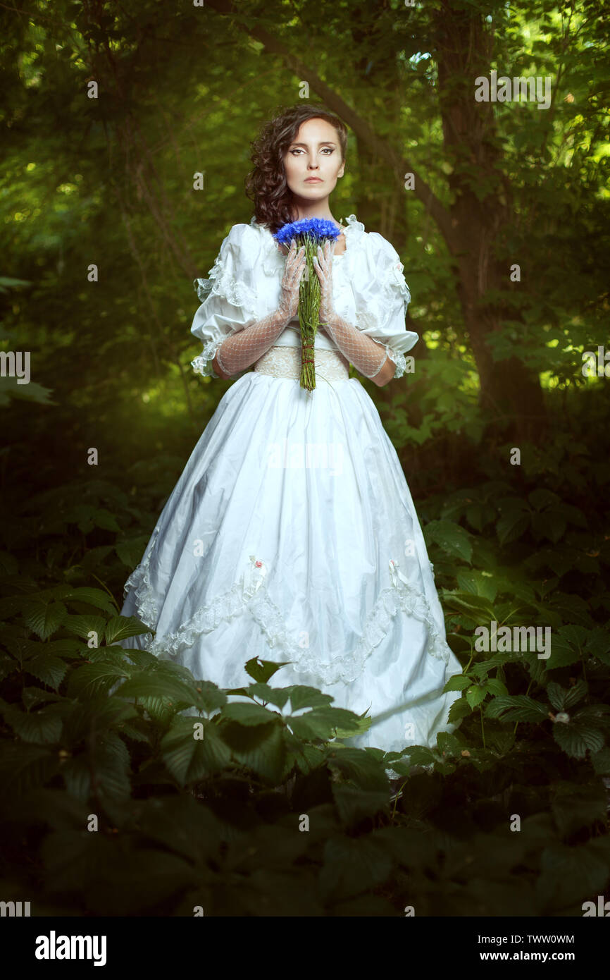 Fantastische Mädchen in einem weißen Kleid mit Blumen Kornblumen im Wald.  Kleid im Retro-Stil. Das Mädchen ist geheimnisvoll und mystisch  Stockfotografie - Alamy