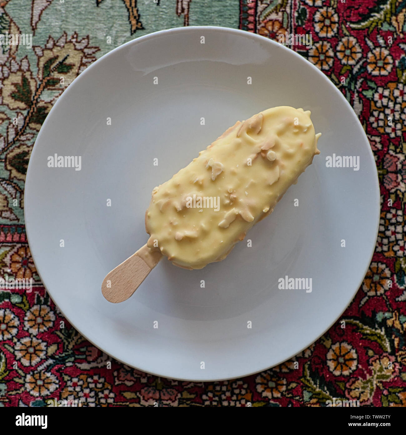 Eisbar mit Nüssen auf einem weißen Teller, fotografiert von oben auf einer gemusterten Tischdecke. Stockfoto