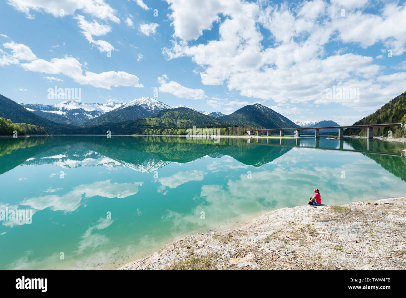 Frau sitzt am Ufer des Sylvenstein Stausee und das Karwendelgebirge im türkisfarbenen Wasser, Bayern reflektiert suchen, Deutschland Stockfoto