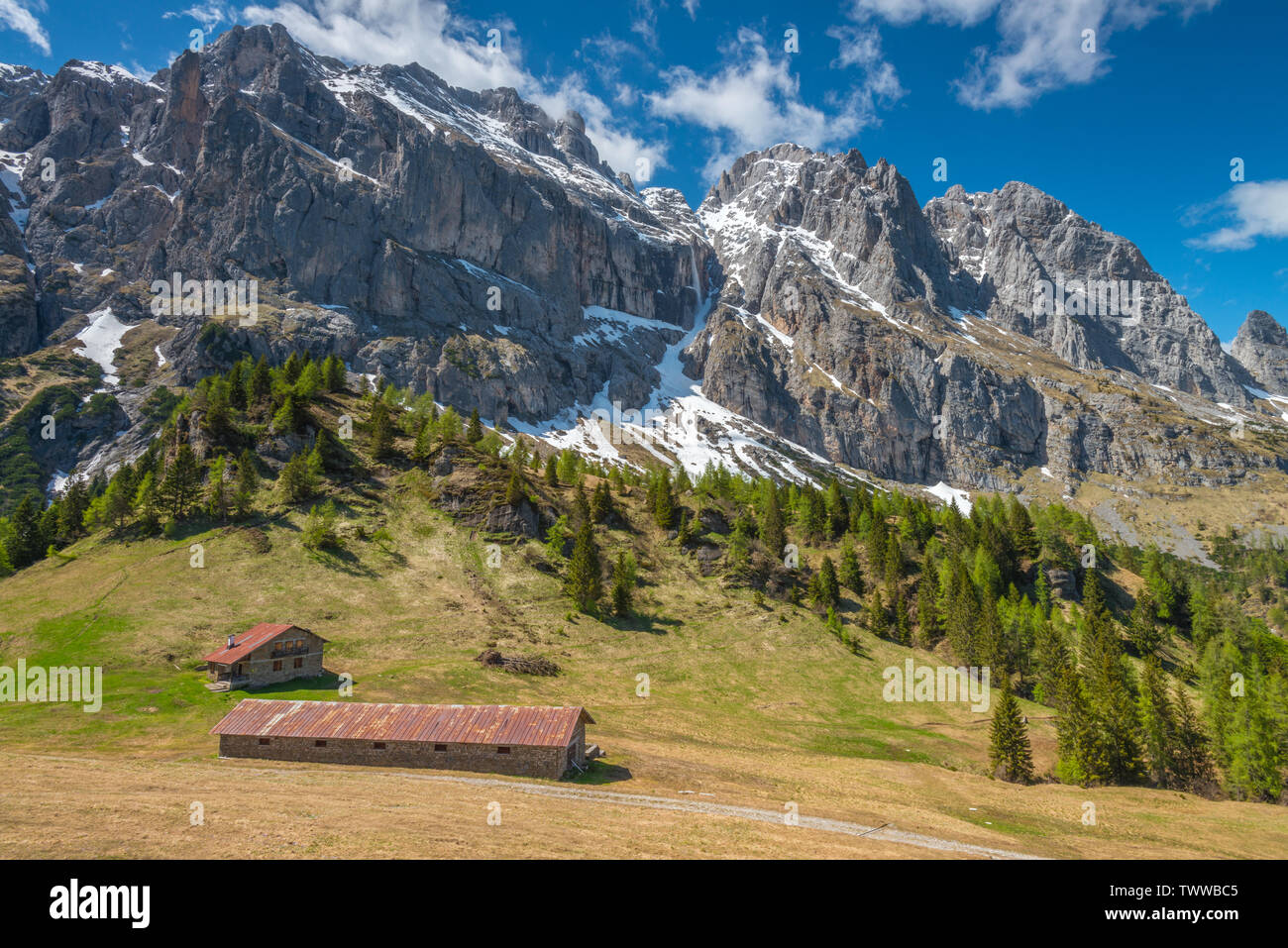 Imposante Bergmassiv ragt über Almen und Schutzhütten im Tal unten. Gefahrenstellen Skipisten in den Dolomiten. Üppigen Weide. Stockfoto