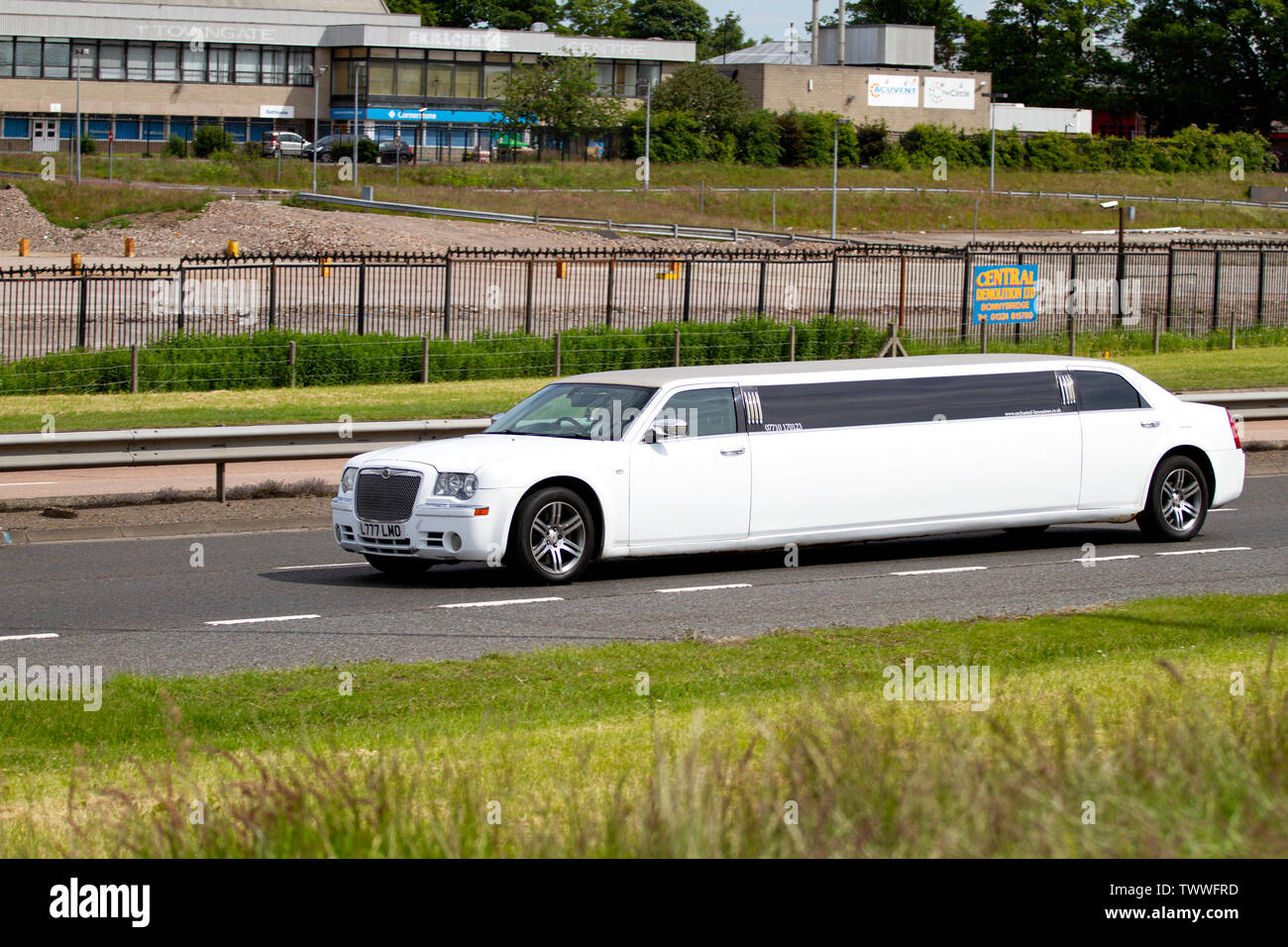 Ein gut gekleideter Chauffeur fahren eine lange weiße Limousine Auto entlang der Kingsway West Zweispurigen Straße in Dundee, Großbritannien Stockfoto