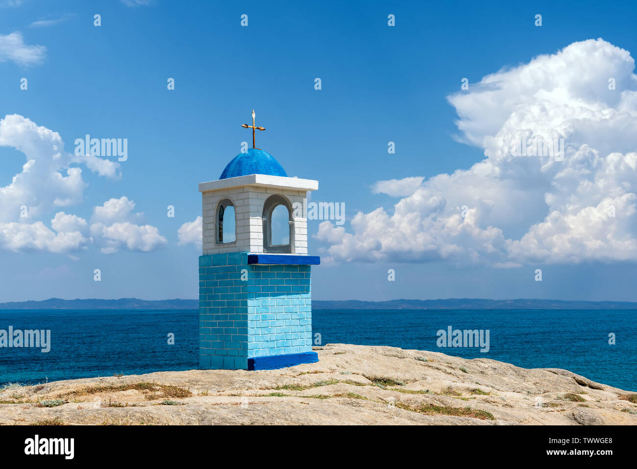 Traditionelle griechische kleine Kirche oder Kapelle. Blauer Himmel mit weißen Wolken und Meer im Hintergrund Stockfoto