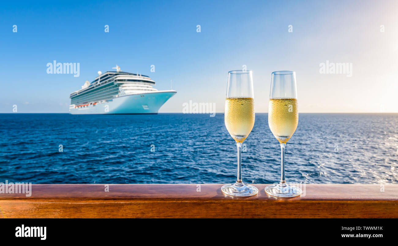 Zwei Gläser Champagner auf hölzernen Geländer bei Sonnenuntergang. Verschwommen Kreuzfahrtschiff in den Hintergrund. Luxus Reisen Urlaub. Stockfoto