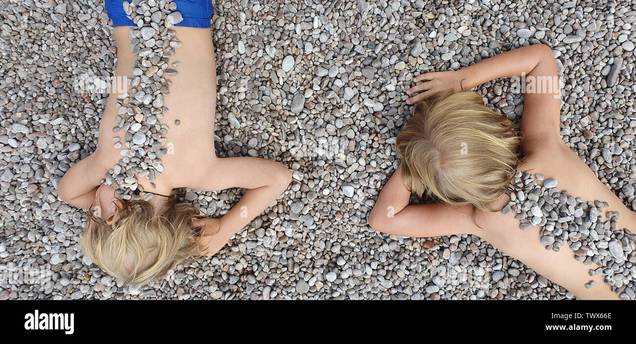 An sonnigen Strand happy Kids Spaß haben, liegen auf heiße Kiesel, Sonnenbaden, Erwärmung nach dem Schwimmen im Meer. Aktive Kinder Lifestyle, Sommer Urlaub Stockfoto