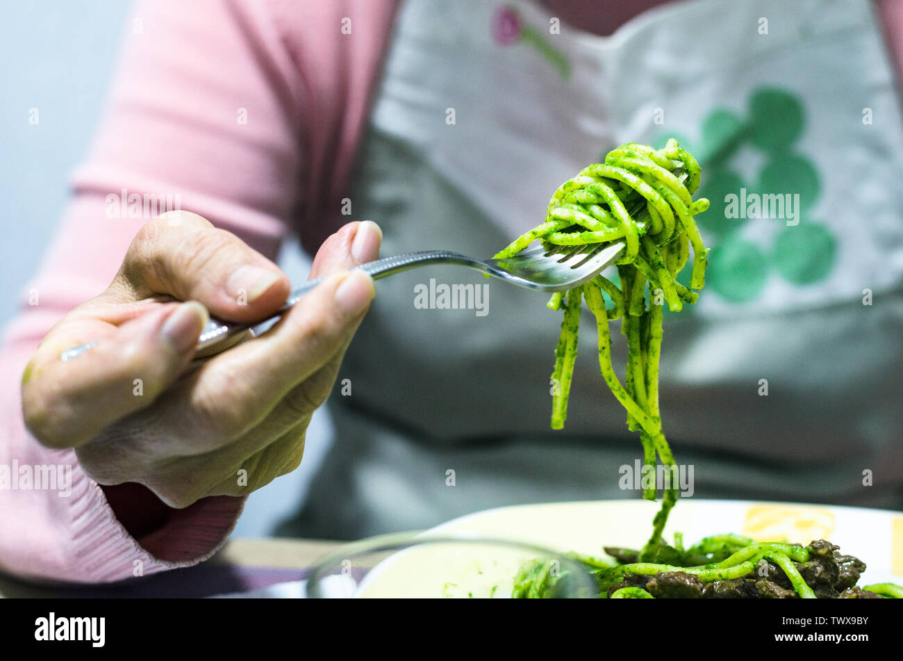 Nahaufnahme der italienischen Pasta Nudeln in grüne Basilikum Sauce und Gabel durch die Hände von einem Koch Frau hielt Stockfoto